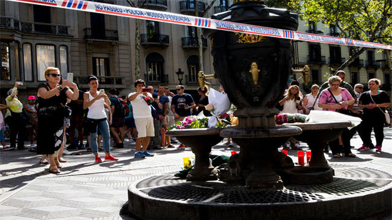 Varias personas fotografían la fuente de Canaletas, en las Ramblas de Barcelona, en la que se han depositado velas y flores en