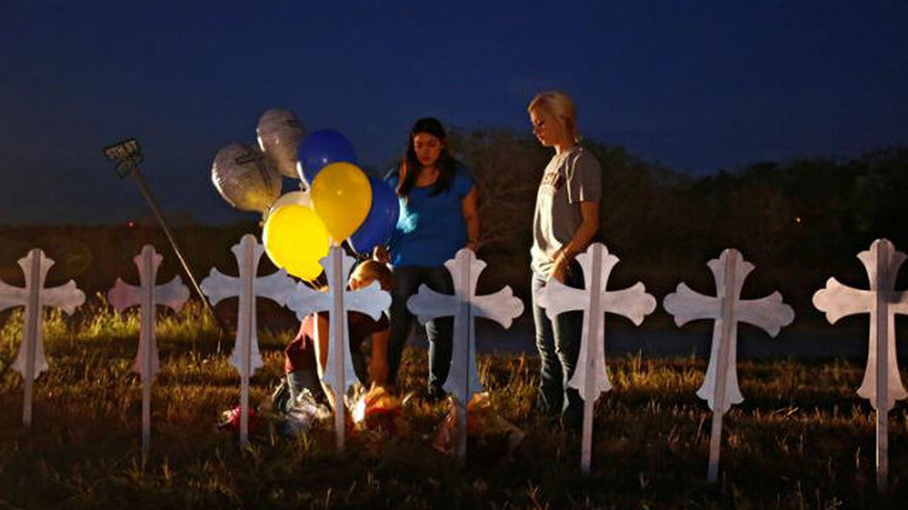 Personas llevan flores y globos a las 26 cruces instaladas en un campo, en honor de las 26 personas que fallecieron luego de un