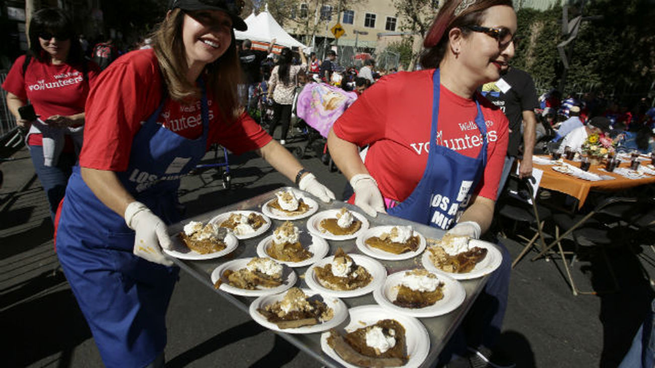 Dos voluntarias cargan platos de comida para repartir durante una comida de Acción de Gracias para personas sin hogar