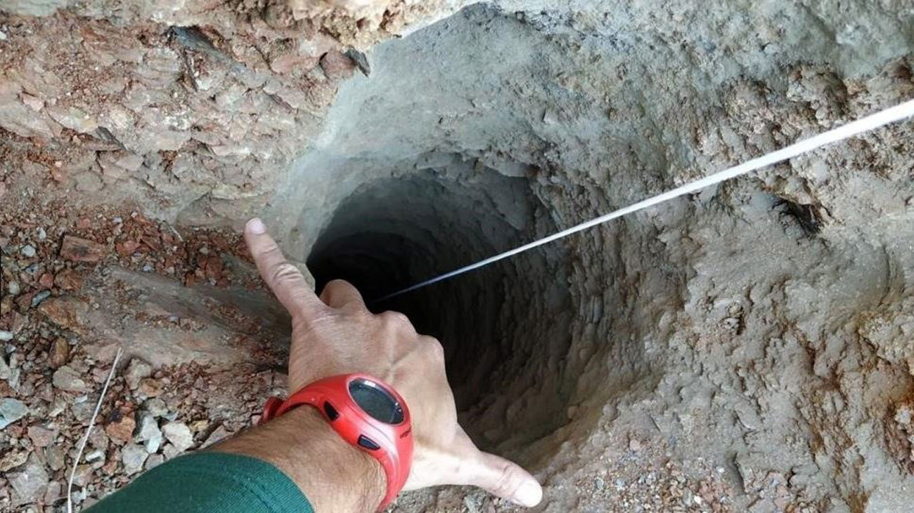 Un guardia civil señala el orificio, de apenas 30 centímetros de ancho, del pozo de más de 100 metros de profundidad por el que cayó un niño de dos años en una finca privada de la localidad malagueña de Totalán