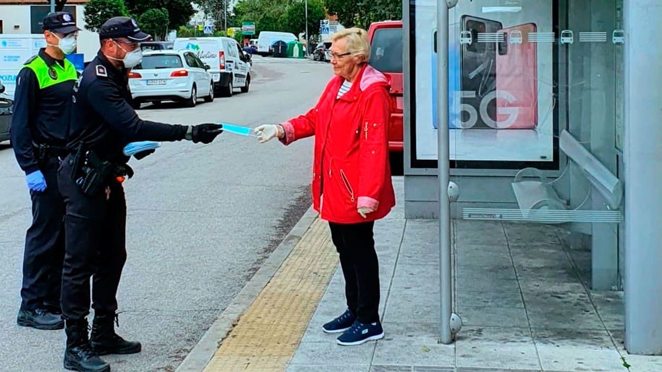 Agentes de la Policía Municipal de Pozuelo de Alarcón reparten mascarillas a una vecina de la localidad.