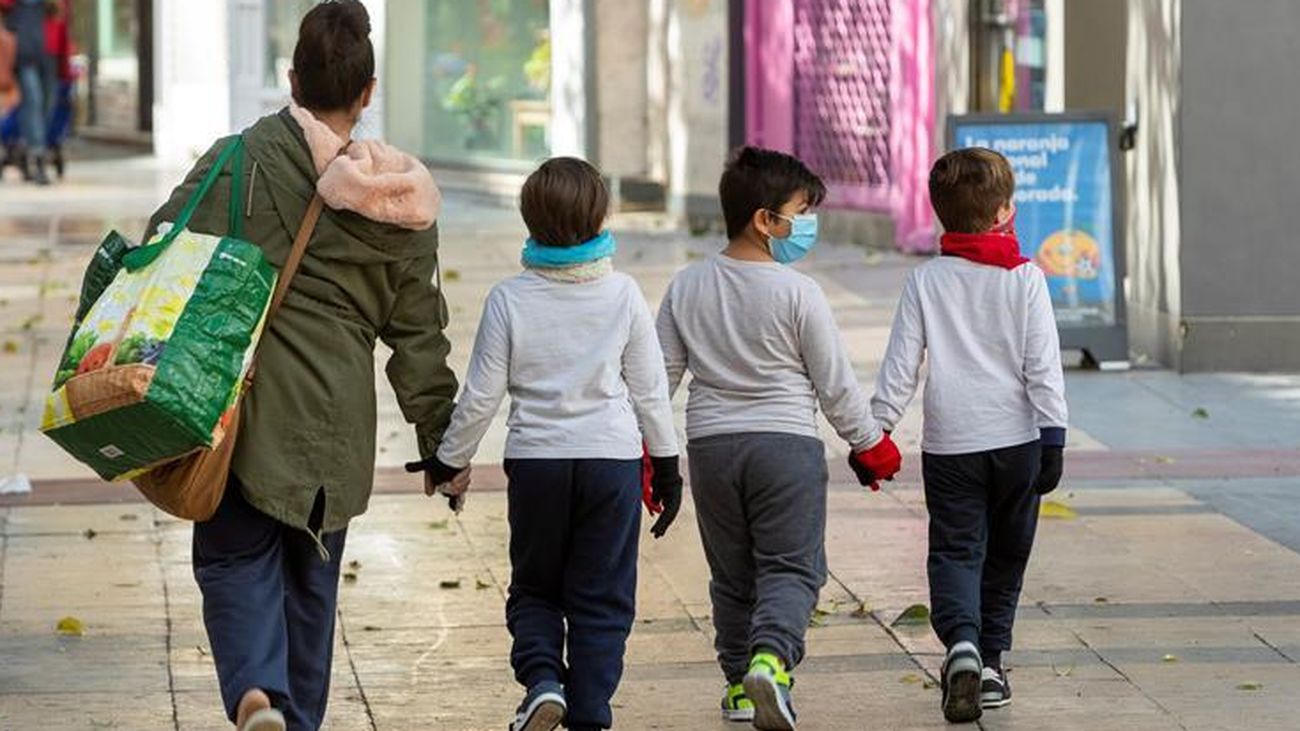 Tres niños caminan por la calle junto a una persona adulta