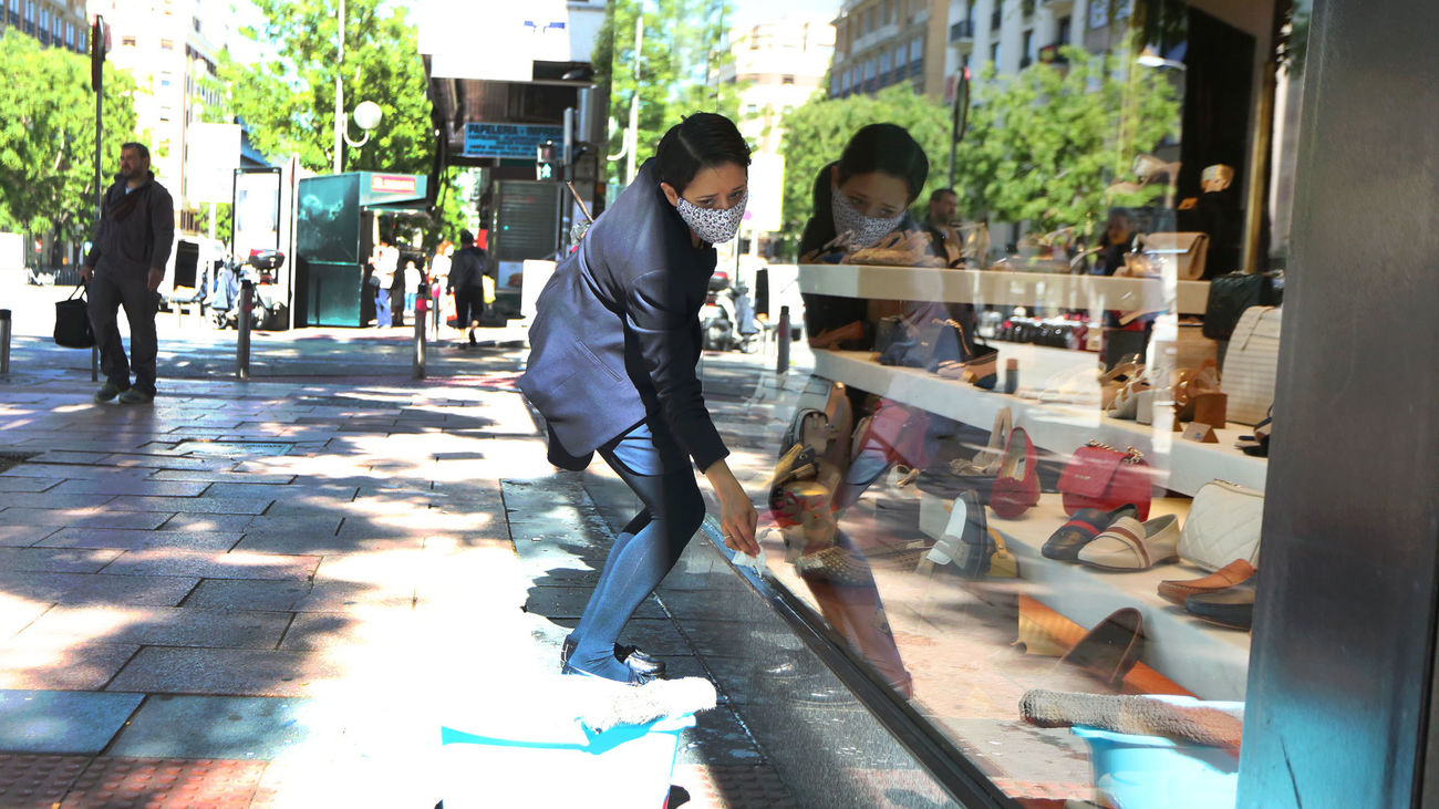 La empleada de una zapatería limpia el escaparate del comercio en la reapertura, tras el parón en la actividad por el estado de alarma