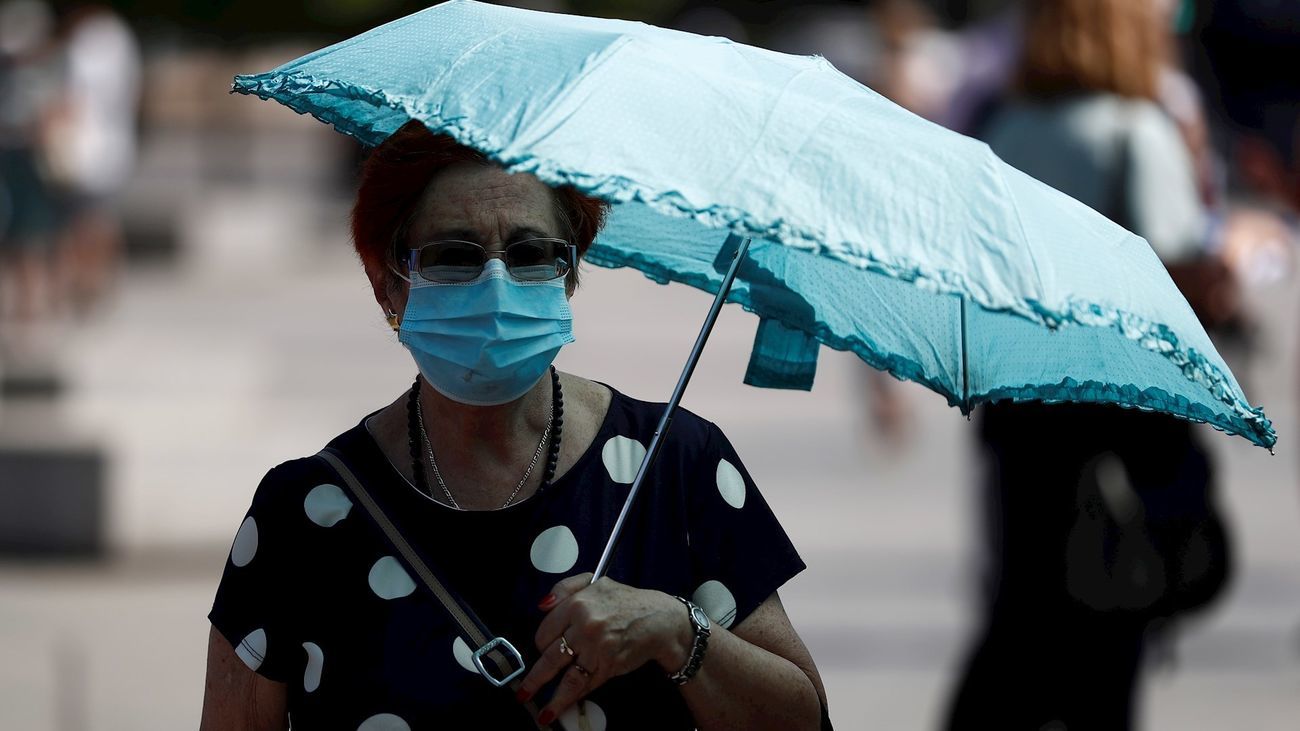 Una mujer pasea con mascarilla y paraguas para refugiarse del calor
