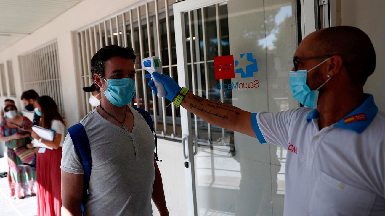 Un sanitario toma la temperatura a una personas que esperan su turno para realizarse una prueba PCR