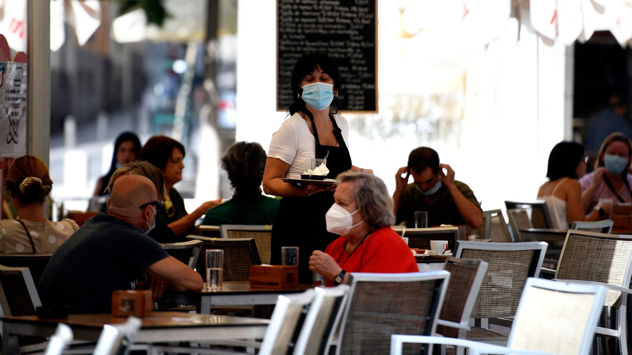 Una camarera con mascarilla atiende a los clientes en una terraza de un bar