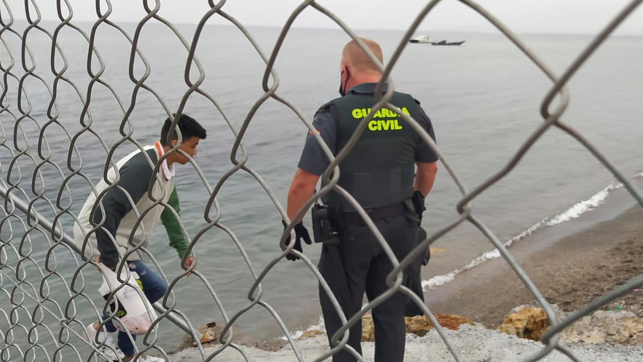 Un Guardia Civil ayuda a uno de los inmigrantes en uno de los espigones fronterizos de Ceuta