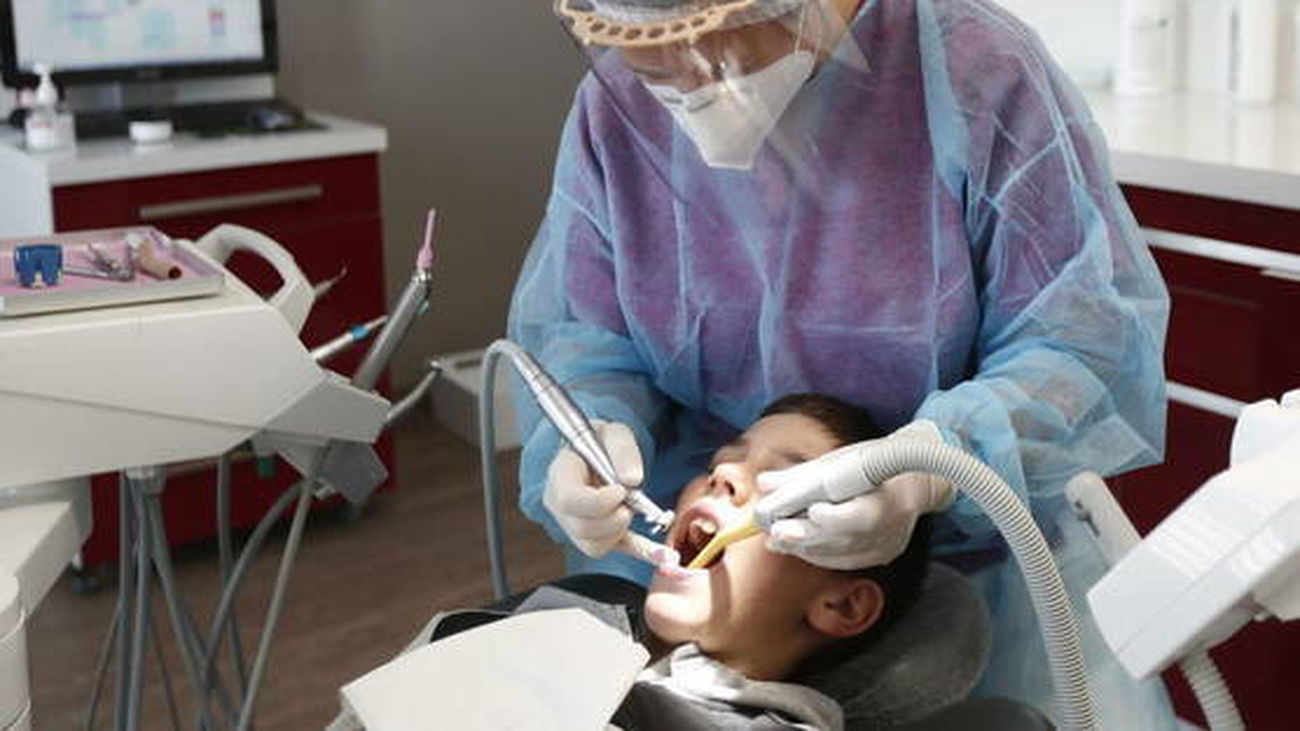 Un odontólogo, con equipo de protección, revisa la dentadura a un niño