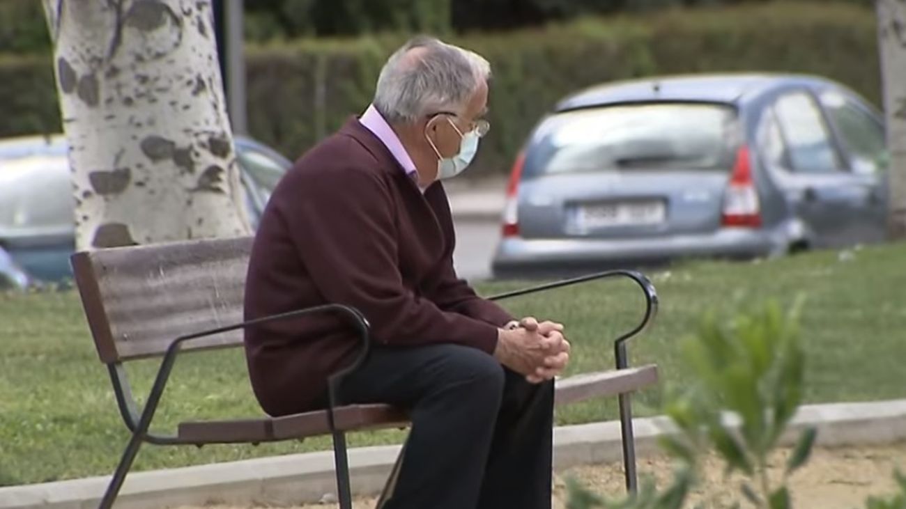 Una persona mayor descansa en un banco de la calle
