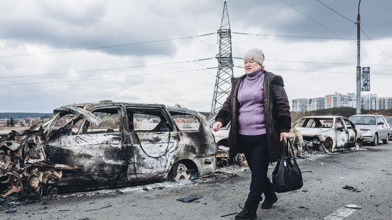Una mujer camina delante de unos coches quemados en un puente de Irpin