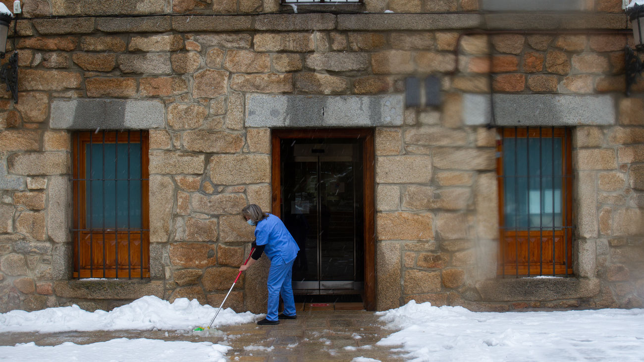 Una mujer despeja la nieve de la entrada del Ayuntamiento de Navacerrada