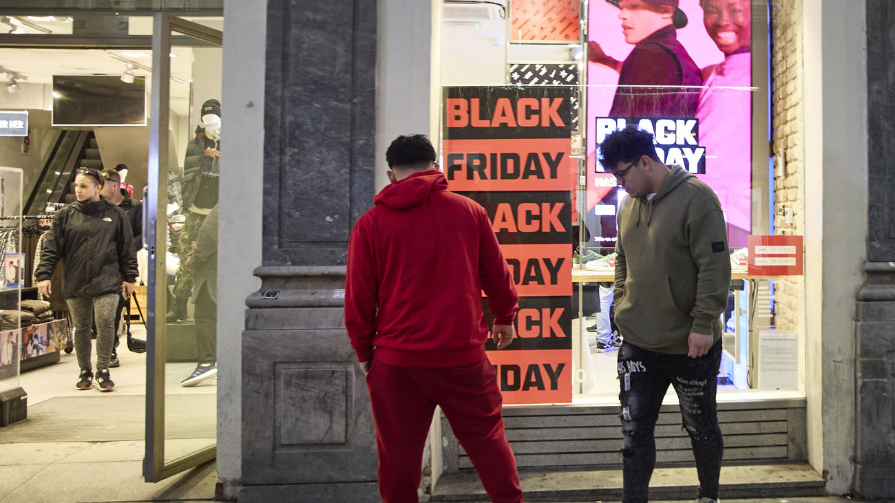 Varias personas pasan por delante de los comercios que anuncian los descuentos del Black Friday