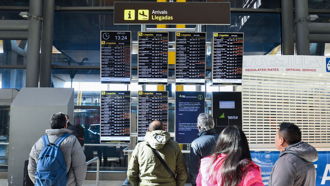 Varias personas observan los paneles informativos que anuncian retrasos de llegadas en algunos vuelos de Iberia en la Terminal 4