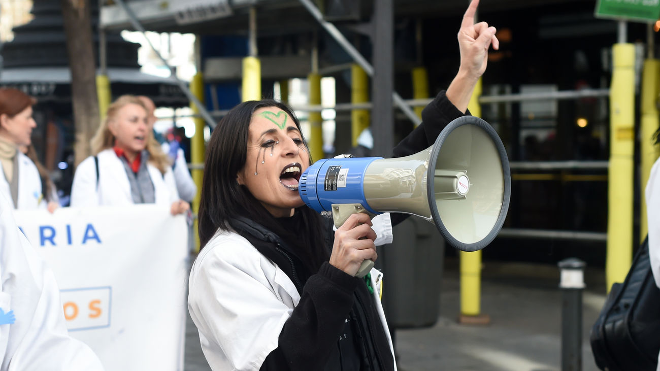 Una mujer con bata blanca sujeta un megáfono durante una concentración de médicos y pediatras de Atención Primaria en huelga