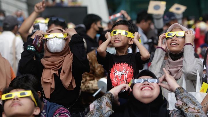 Personas en Yakarta contemplando el eclipse solar híbrido / EFE