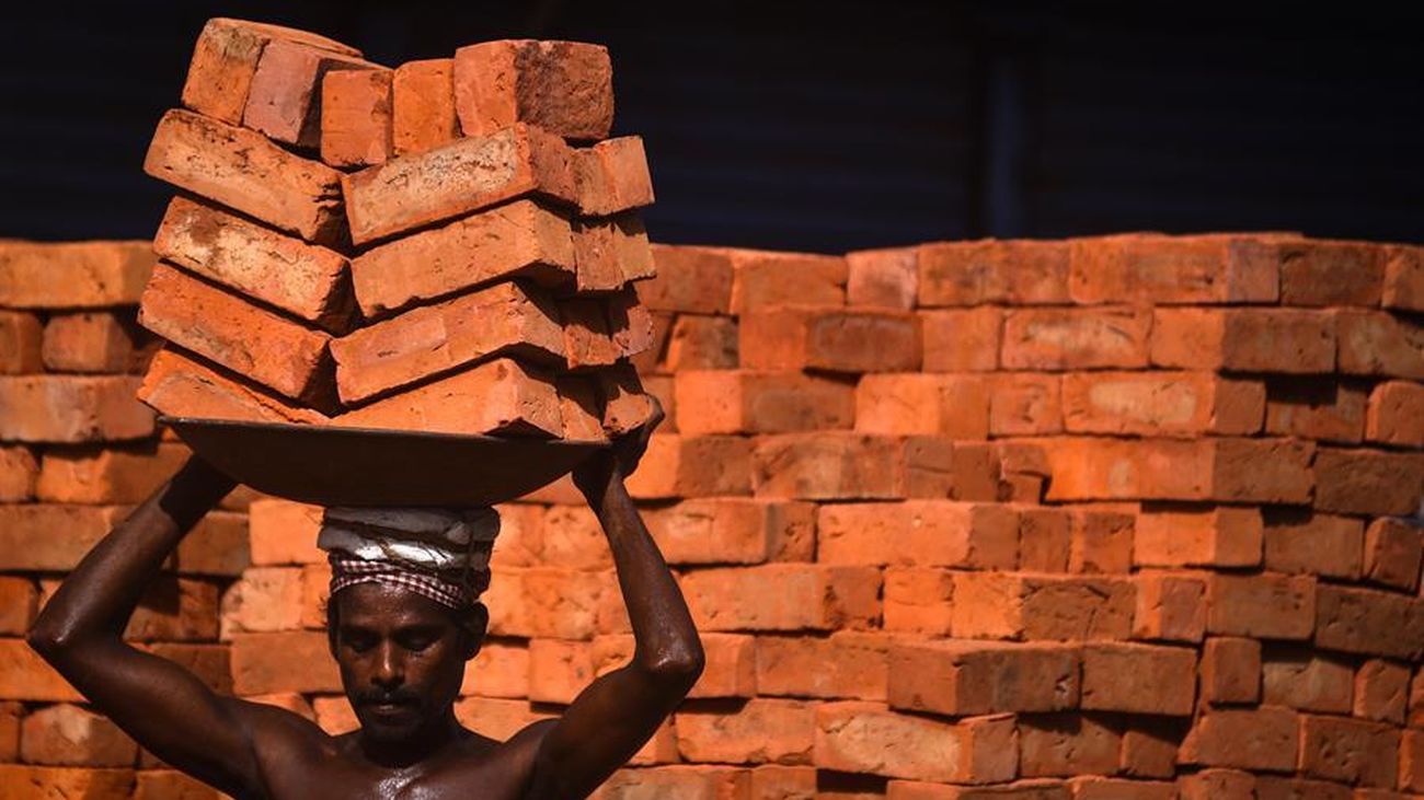 Un obrero indio transporta ladrillos en un complejo comercial en construcción