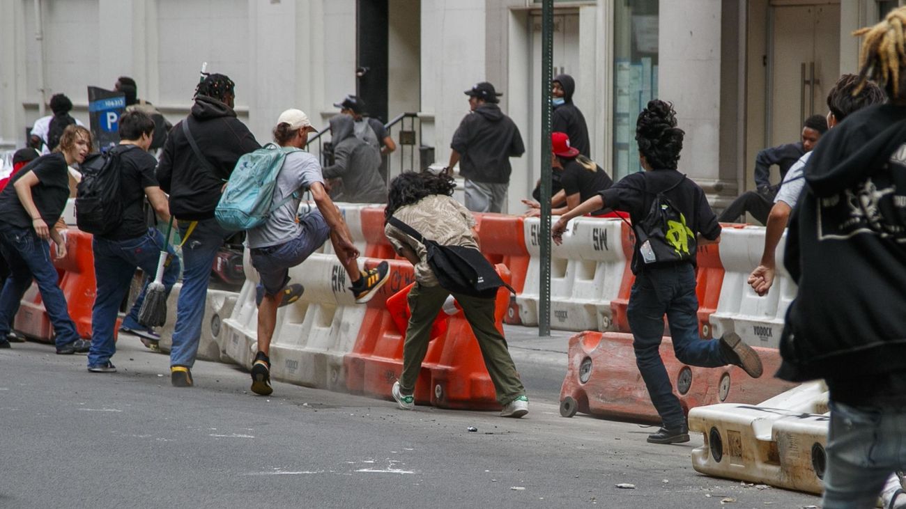 Un grupo de personas derriba a patadas las barreras de construcción durante los disturbios