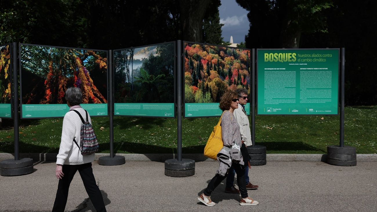 Varias personas pasan por delante de la inauguración de la exposición fotográfica 'Bosques, nuestros aliados contra el cambio climático', 'Casa de Fieras' del Retiro, 30 de mayo de 2023, en Madrid (España)