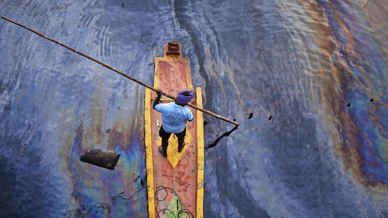 Un pescador indio navega sobre un arroyo cubierto por un derrame de petróleo