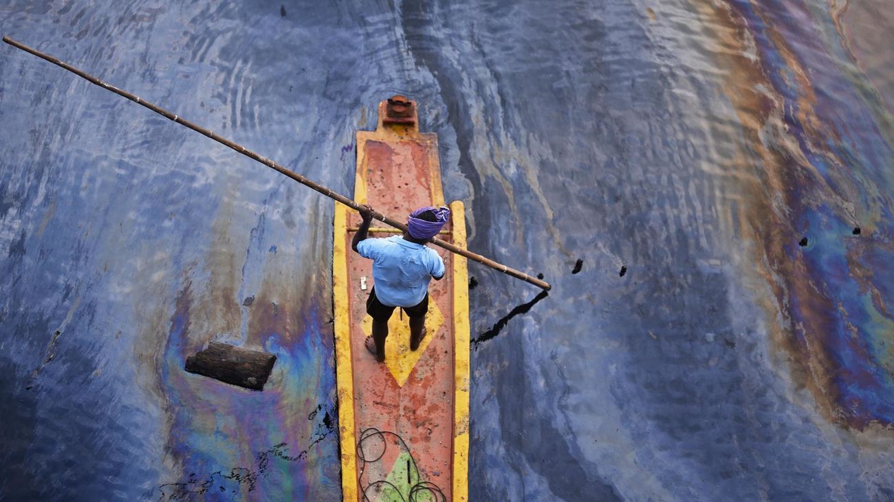 Un pescador indio navega sobre un arroyo cubierto por un derrame de petróleo