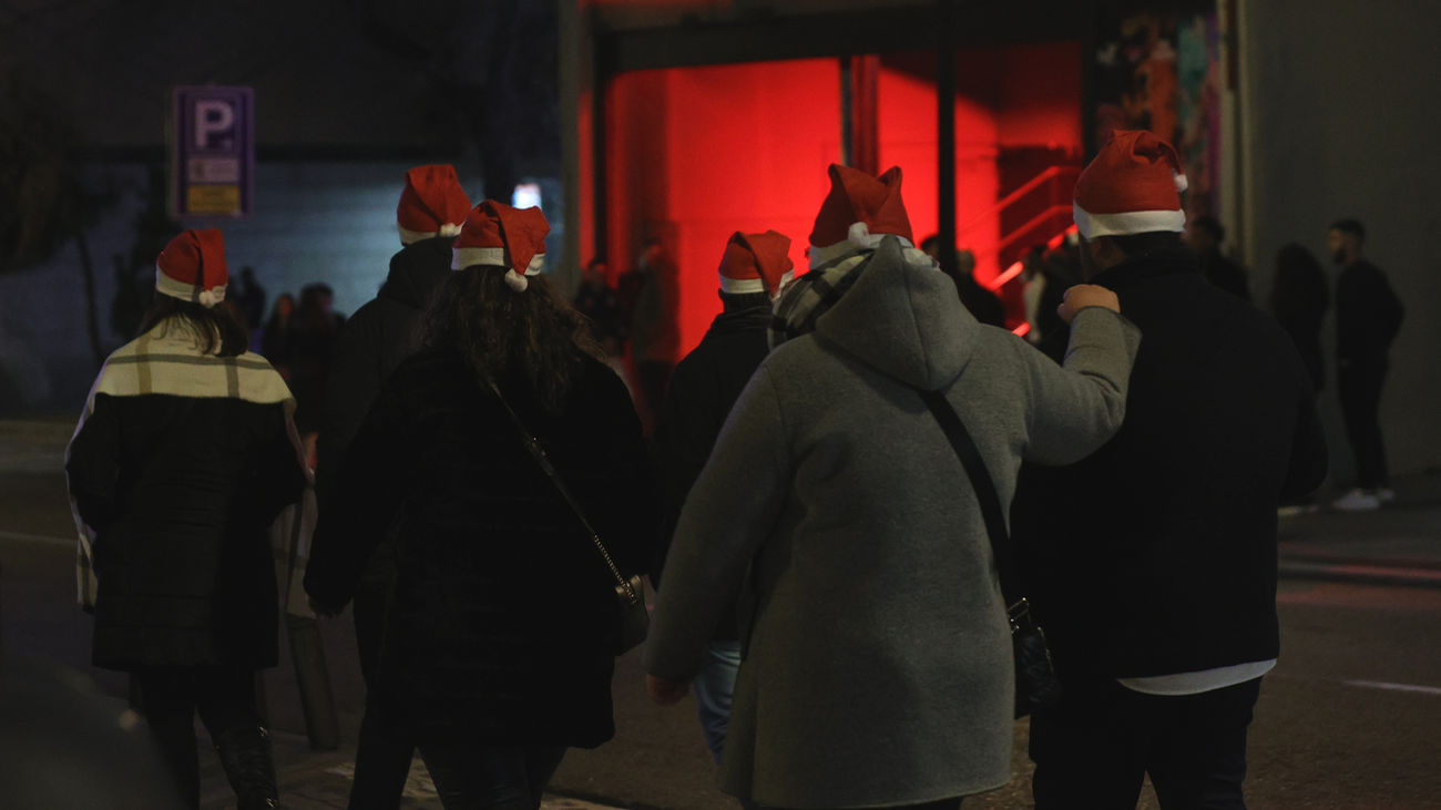 Un grupo de personas pasa por delante de una cola de gente que espera para entrar a una fiesta de Nochevieja