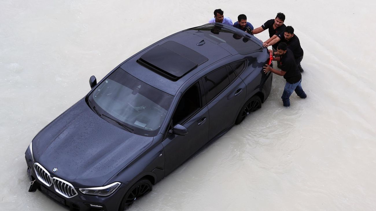 Varias personas empujan un coche averiado a causa de las lluvias en Dubai