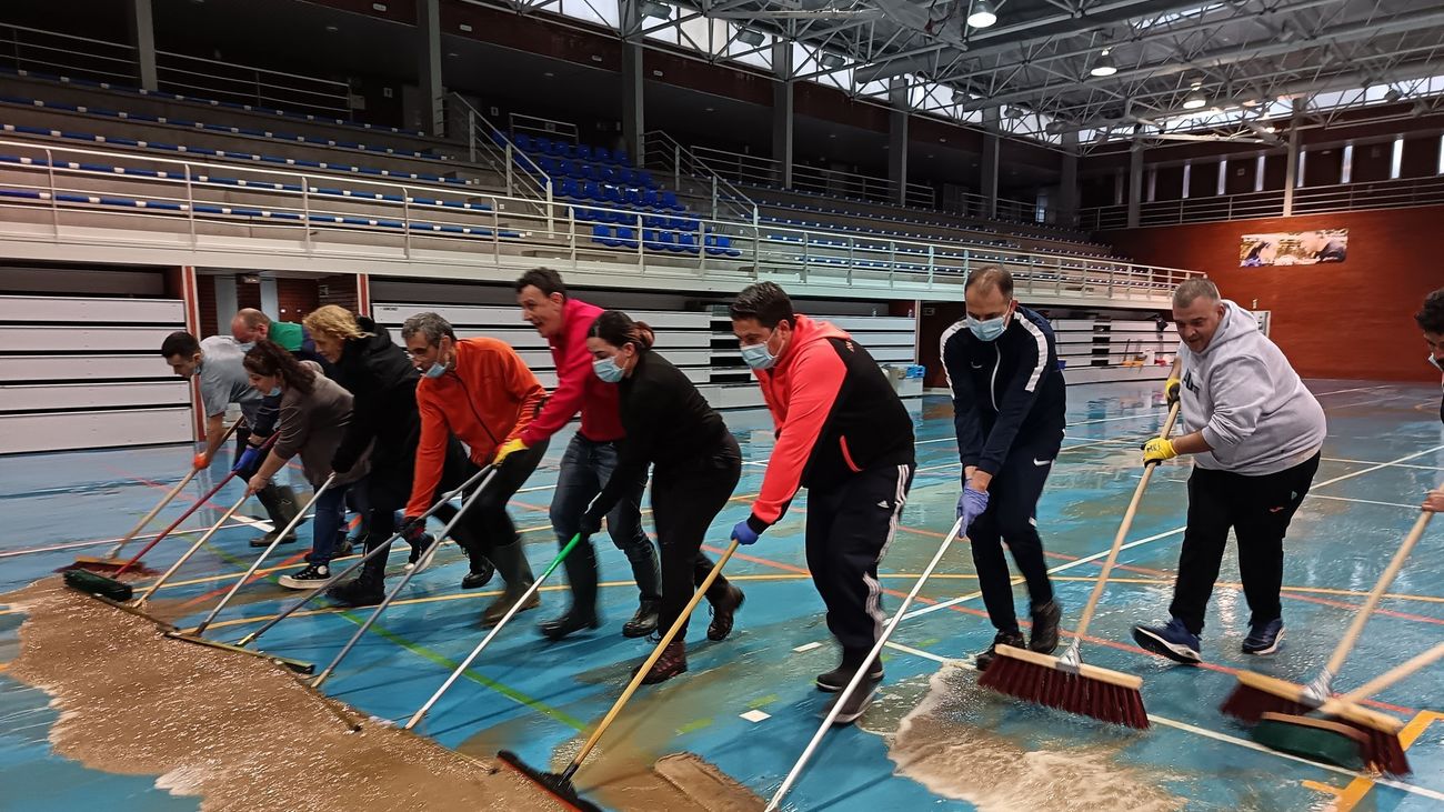 Varias personas retiran agua y barro del polidportivo de San Fernando de Henares