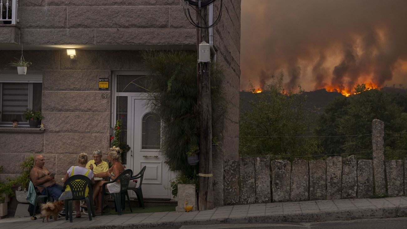 Un grupo de personas juega a las cartas mientras avanza el incendio forestal en Carballeda de Avia, Galicia