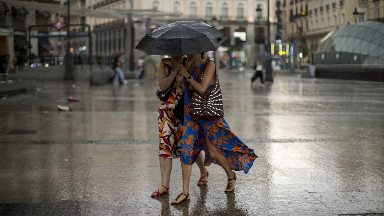 Dos mujeres se cubren de la lluvia con un paraguas en la Puerta del Sol de Madrid