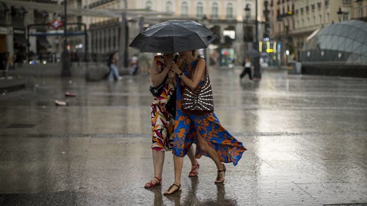Dos mujeres se cubren de la lluvia con un paraguas en la Puerta del Sol de Madrid