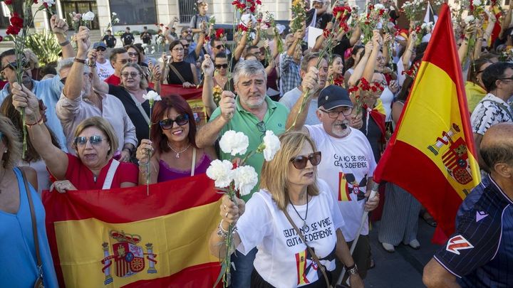 Numerosas personas portan claveles y banderas de España durante una manifestación ante la Delegación del Gobierno en Ceuta