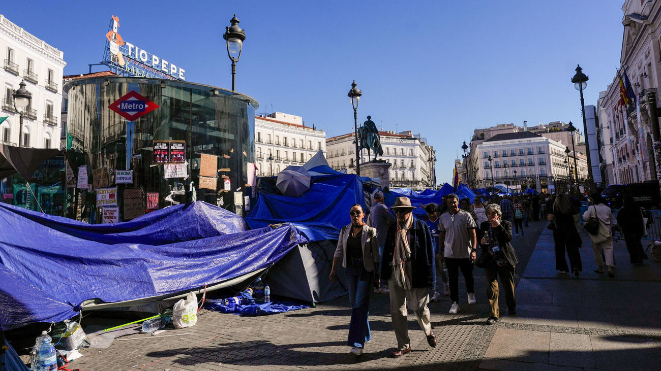 Transeúntes caminan junto a la acampada protesta contra la crisis de la vivienda en la Puerta del Sol