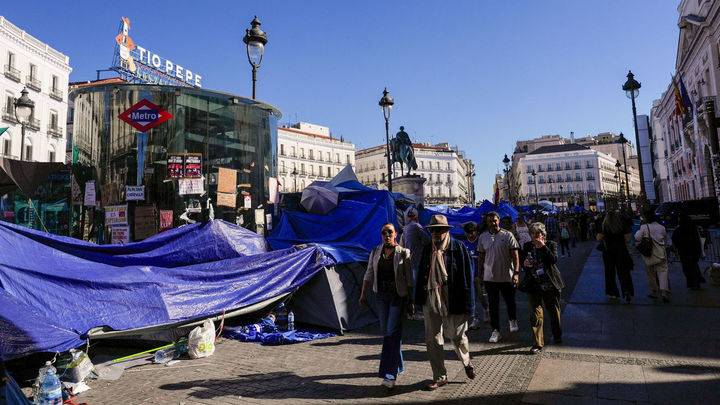 Transeúntes caminan junto a la acampada protesta contra la crisis de la vivienda en la Puerta del Sol